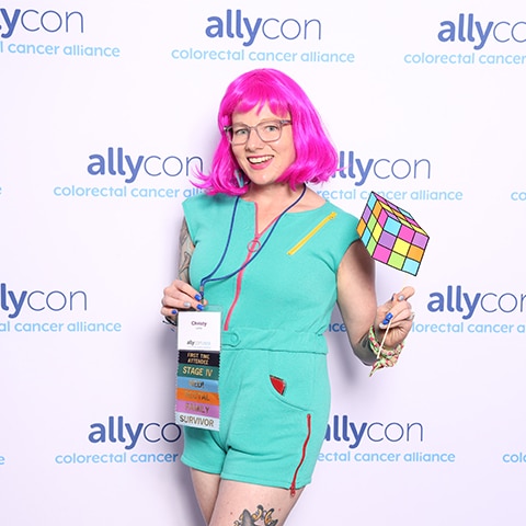 Woman with pink hair posing in front of a custom printed backdrop for Allycon